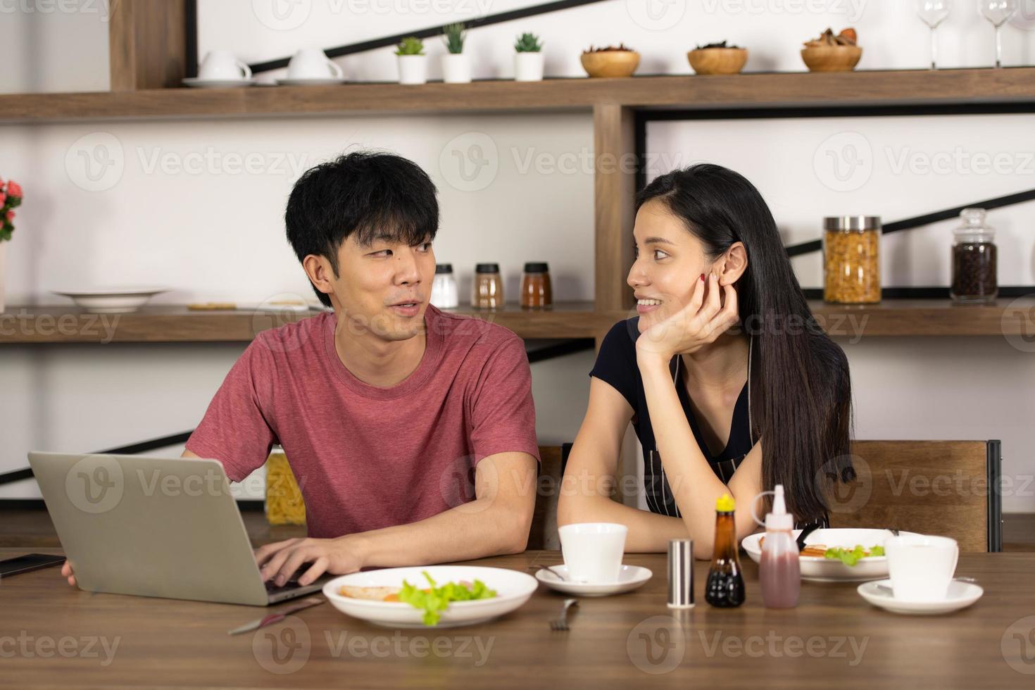 A young Asian couple are eating together and smiling happily while cooking their salad in the kitchen. photo