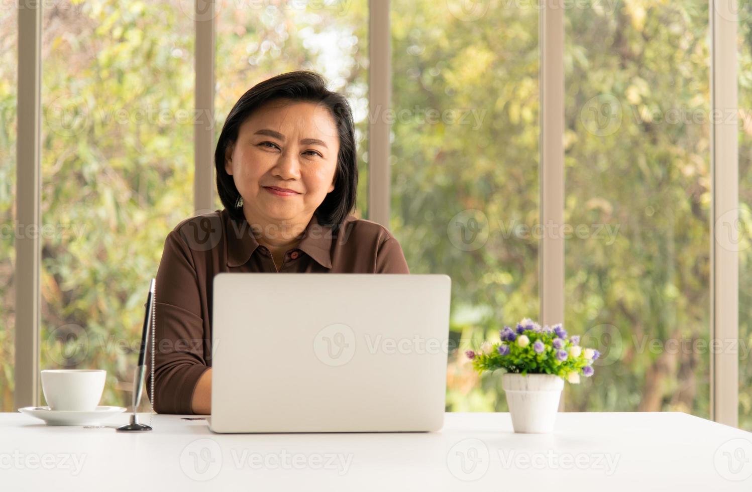 Senior Asian woman using a mobile phone and a laptop in the natural living room background with modern technology photo