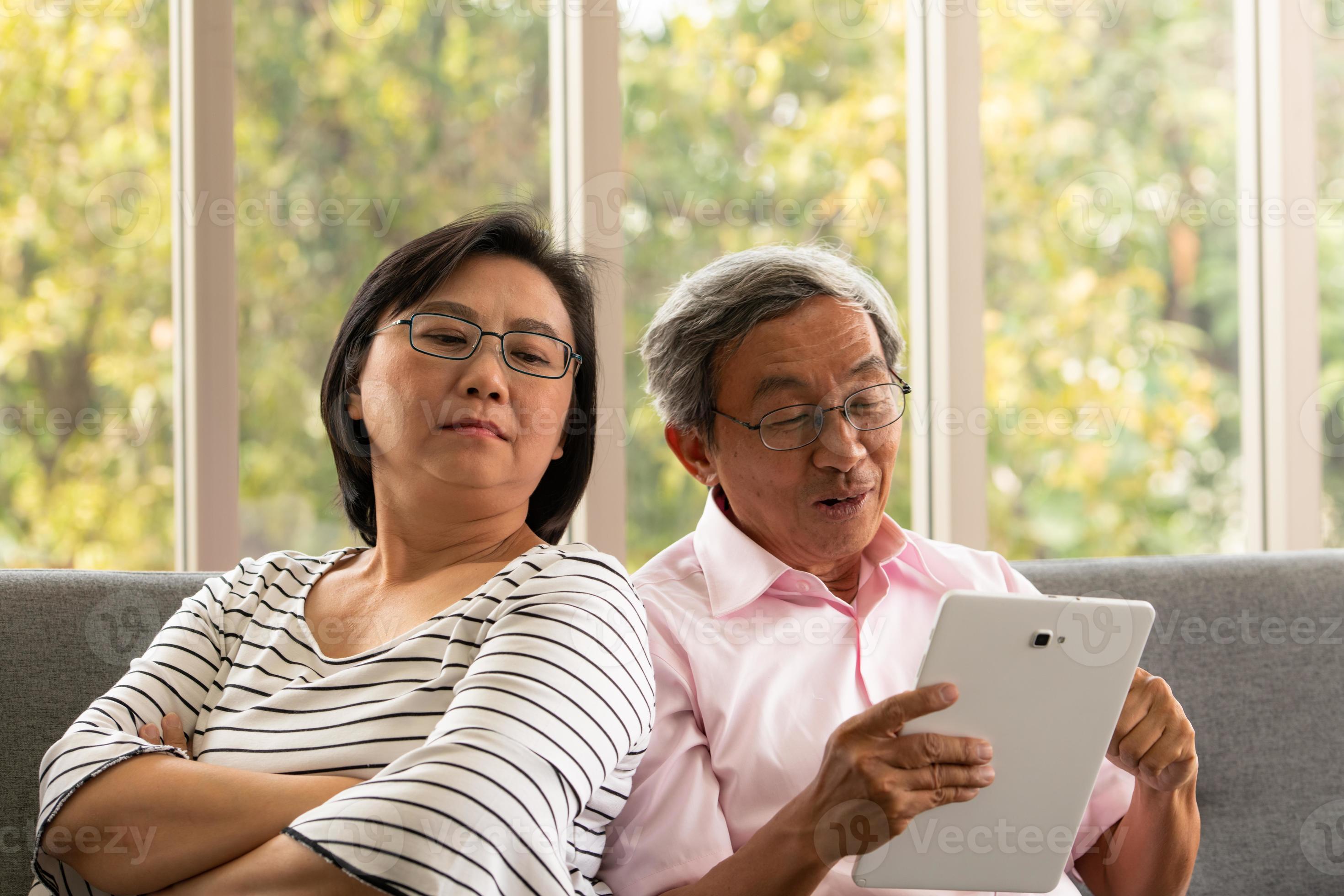 Senior Asian man and woman relax on holiday in the natural living room background with modern technology photo