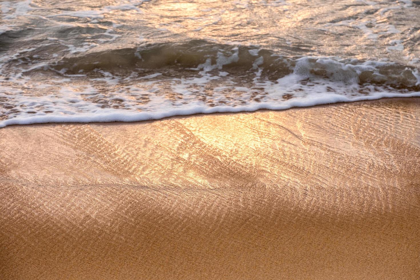 Shiny tropical sea wave with bubble on brown beach at sunset photo