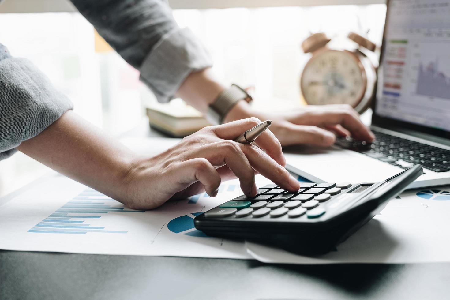 Cerca de la mano del empresario o contador que sostiene la pluma trabajando en la calculadora para calcular datos comerciales, documentos contables y computadora portátil en la oficina, concepto de negocio foto