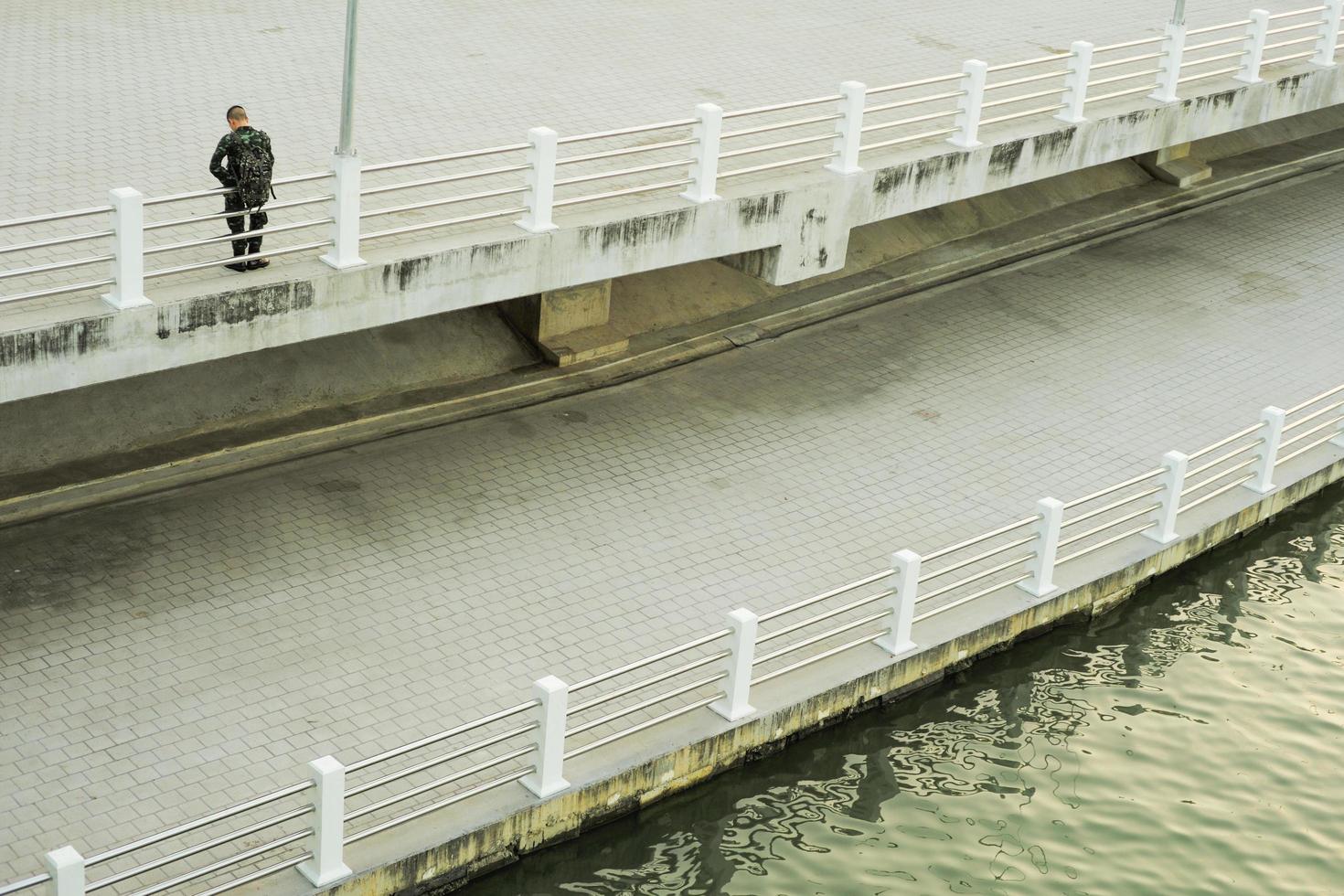 An unidentified man stands on the concrete walkway along the bank of the river with the reflection of the light of sunset. photo