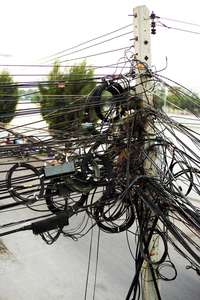 Cables desordenados en un poste de hormigón de electricidad al lado de la carretera en la ciudad foto