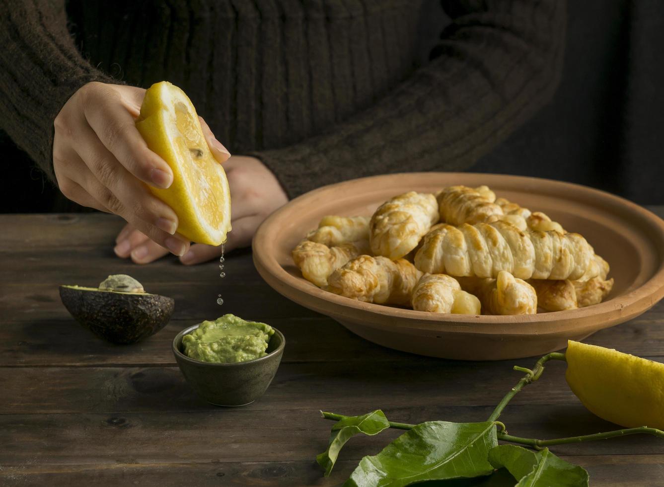 persona exprimiendo jugo de limón en salsa de aguacate con tequenos foto