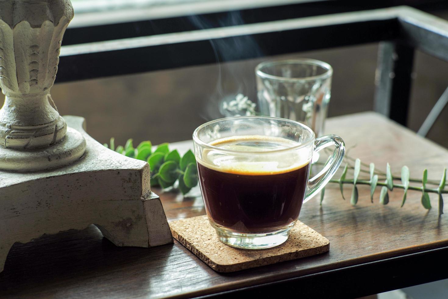 Primer plano de un vaso de café negro caliente con humo sobre una mesa de madera foto