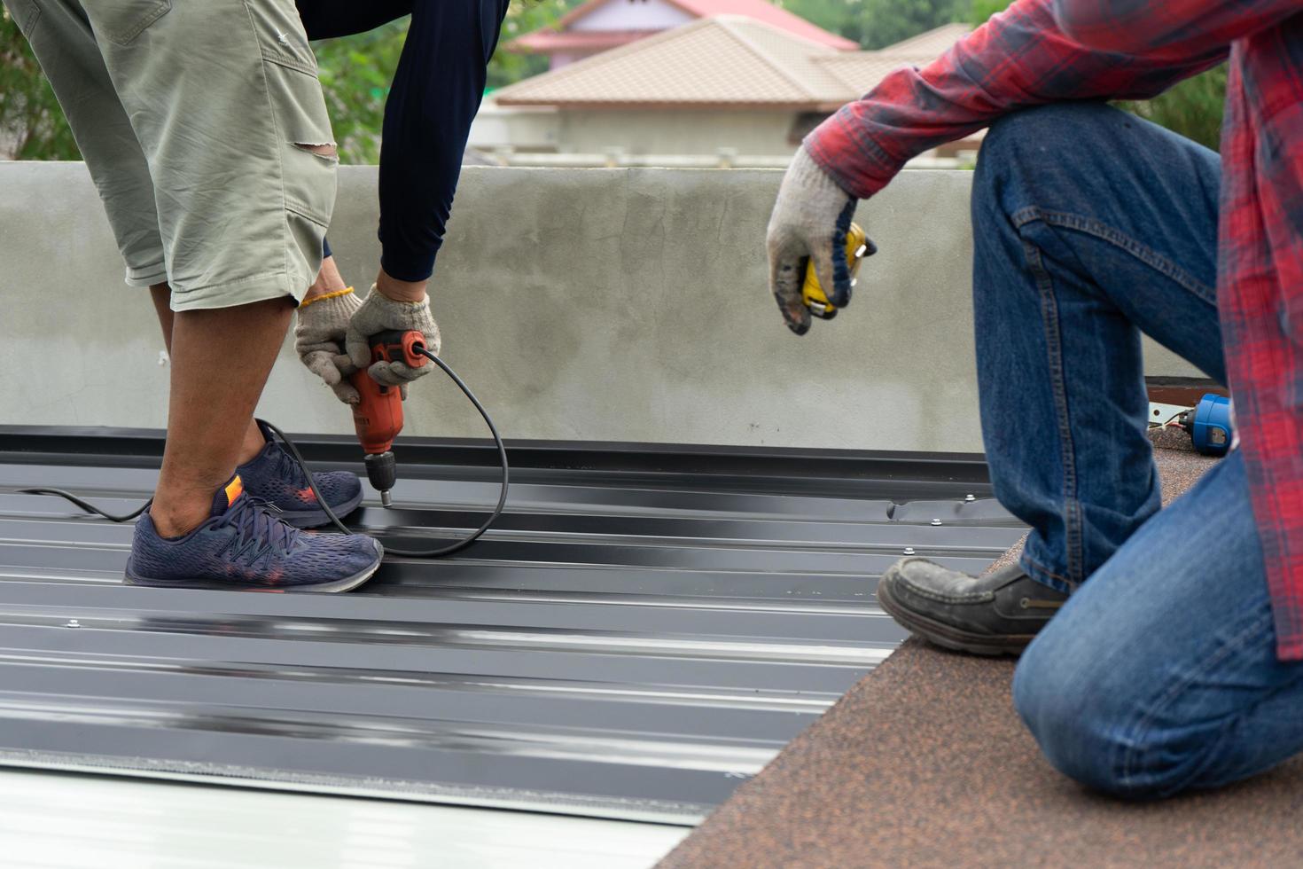 Workers installing a metal sheet roof with an electrical drilling machine. Selective focus on the drilling tool while building the roof photo