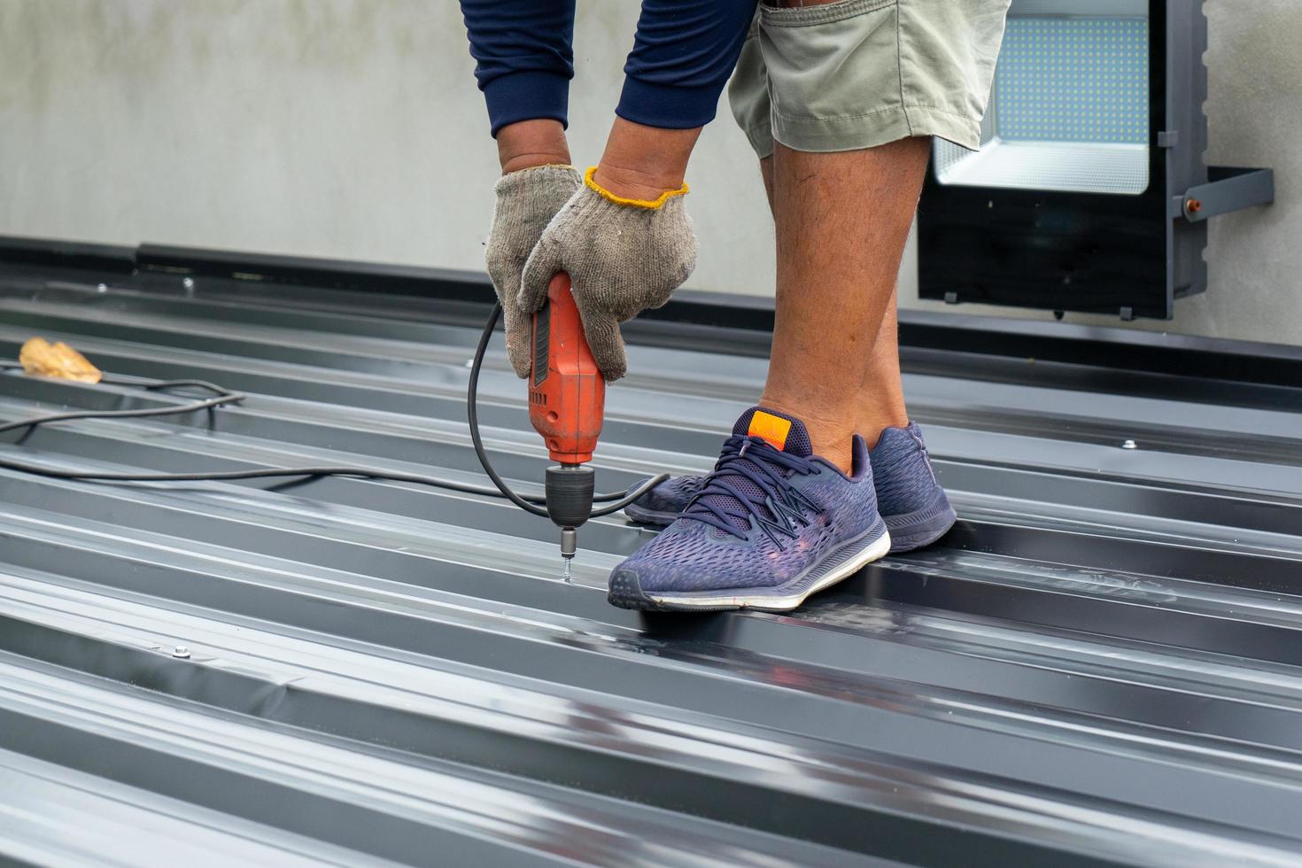 Closeup of hands installing a metal sheet roof with an electrical drilling machine. Selective focus on the drilling tool while building the roof photo