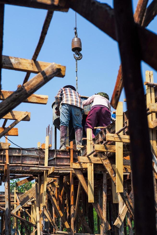 High-angle view of a group of workers pouring mixed cement from a big steel bucket hanging from a crane. photo