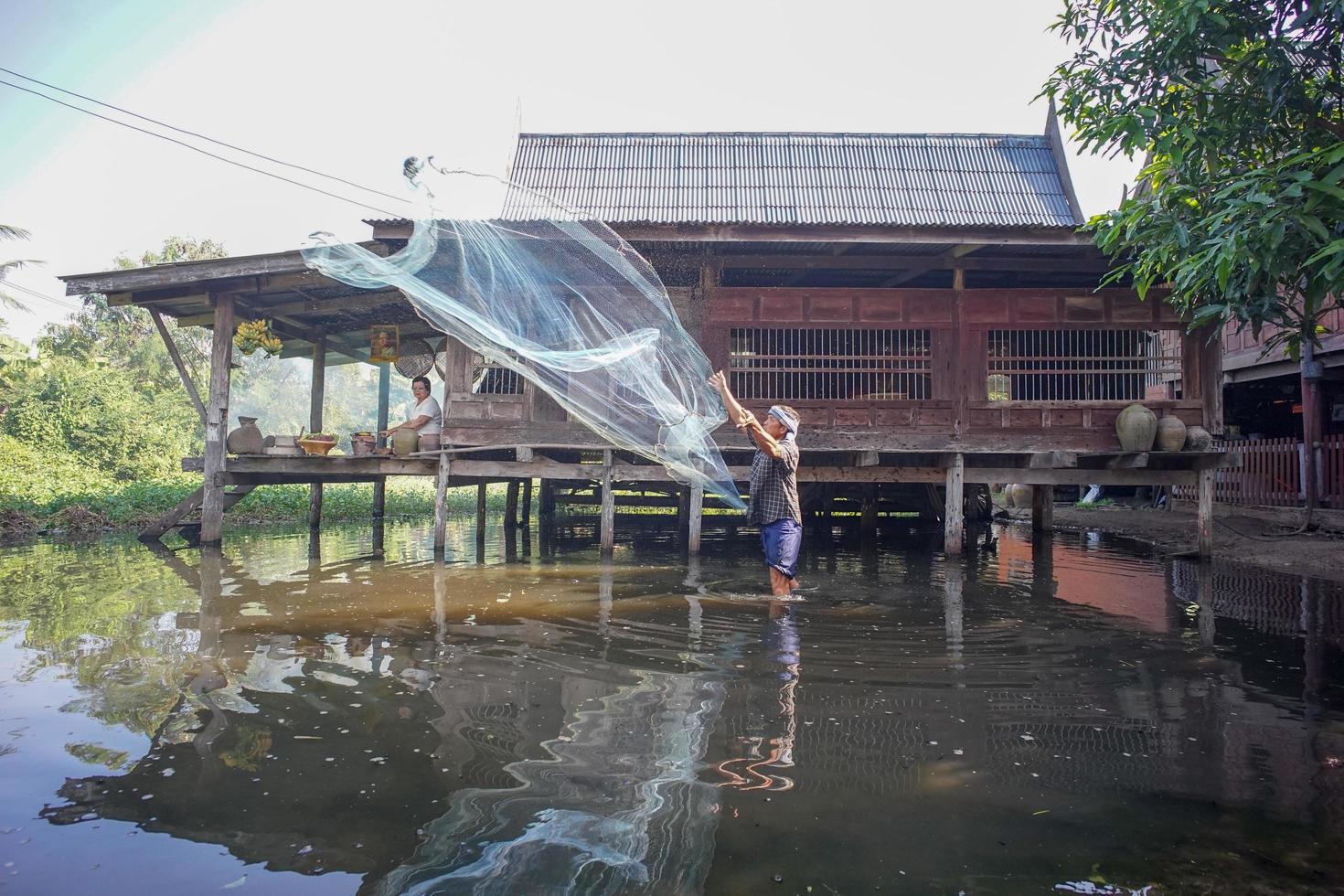 Ratchaburi, Thailand - November 25, 2018 - Lifestyle of Thai folk people in an urban area. A man catching fish with a nylon net in a shallow pond. The memorial of King Rama IX photo