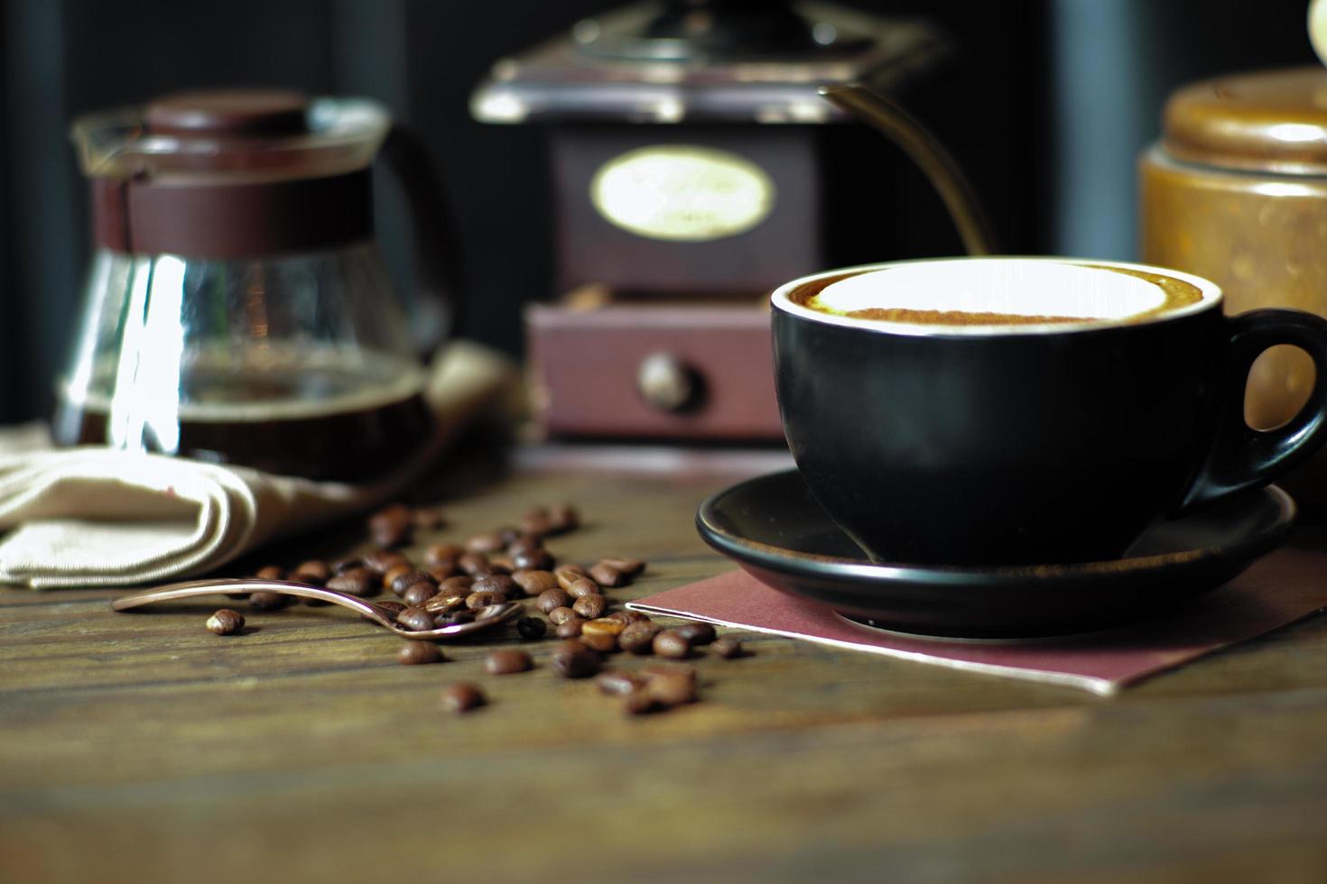 Primer plano de una taza de capuchino caliente con enfoque selectivo en los granos de café en una mesa de madera con fondo molinillo borrosa foto