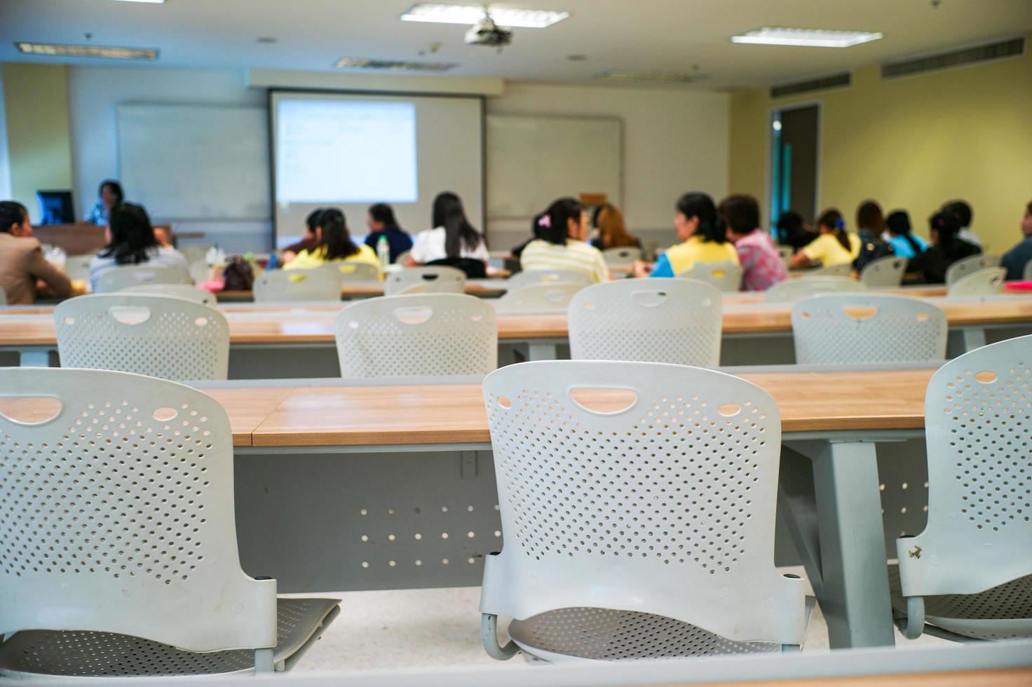 El enfoque selectivo en la fila de sillas vacías con un grupo de estudiantes borrosa en segundo plano. foto