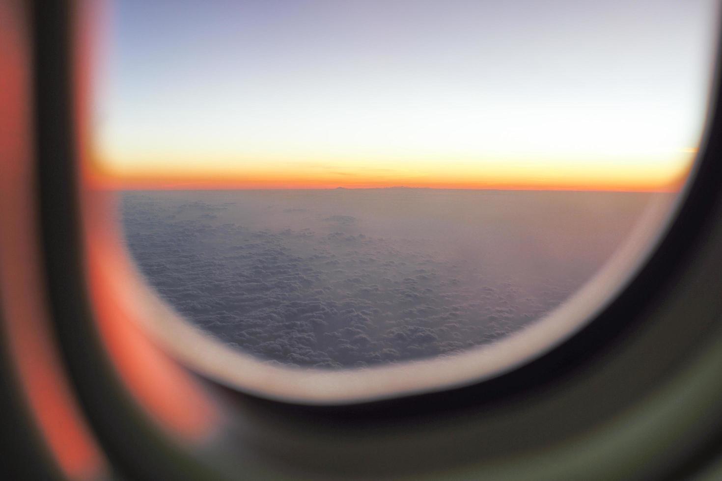La luz del atardecer en el horizonte con fondo de cielo azul y la sombra de la ventana de un avión en primer plano foto