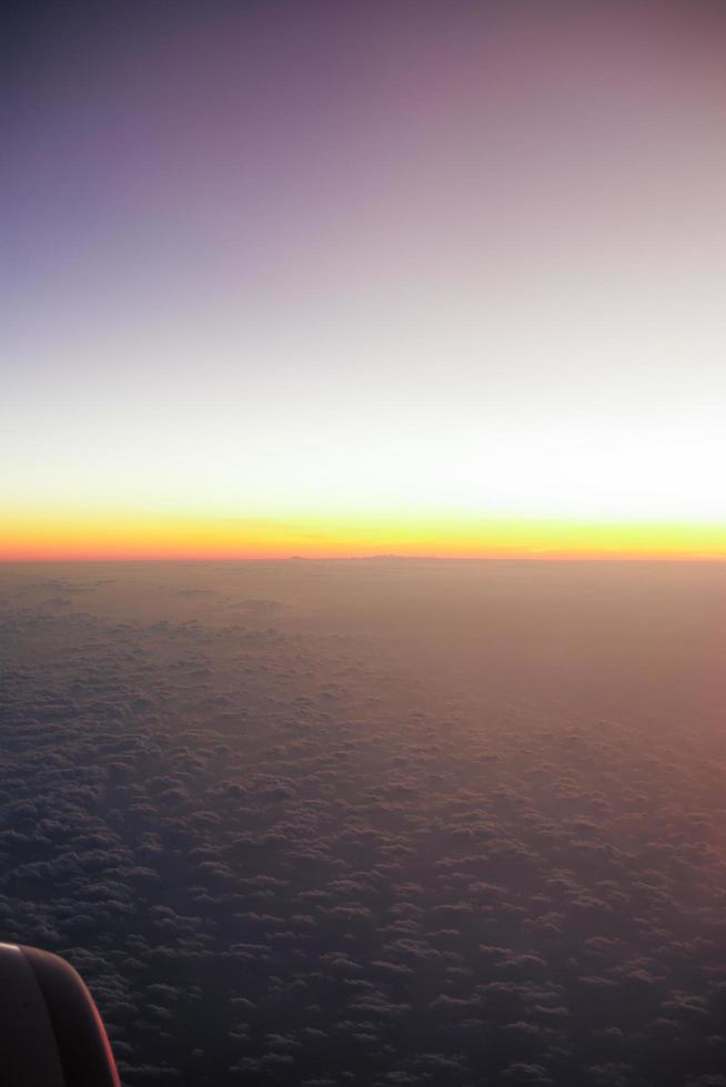 La luz del atardecer en el horizonte con fondo de cielo azul y la sombra de la ventana de un avión en primer plano foto