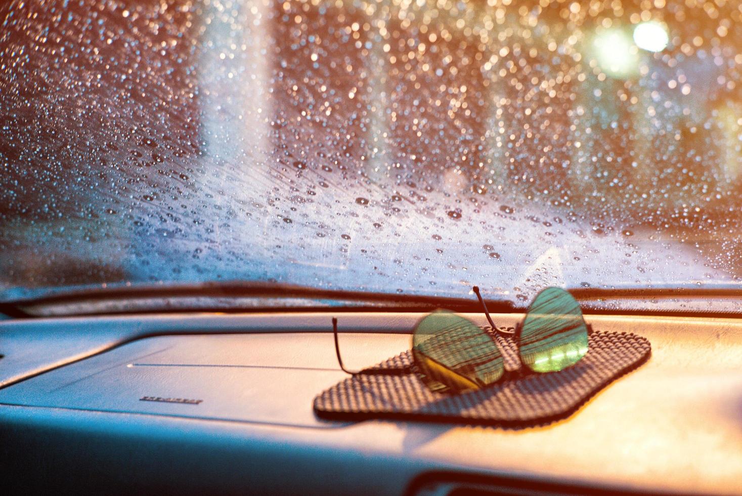 gotas de lluvia y humedad en el cristal delantero del coche con gafas de sol borrosas en primer plano. foto