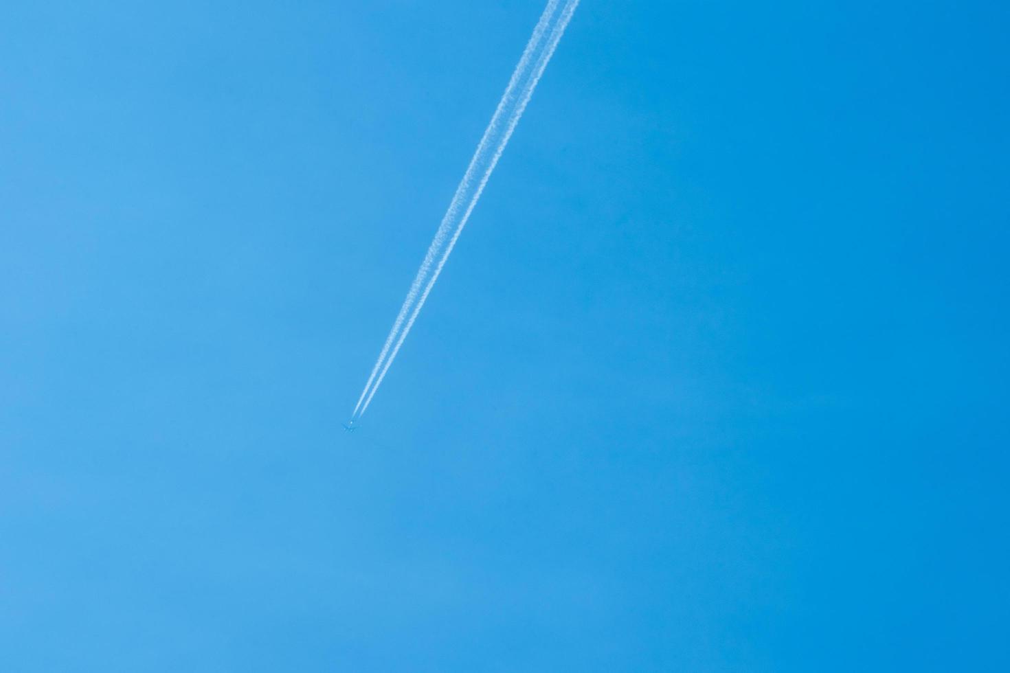 Avión volando en el cielo azul claro con rastro blanco a lo largo de la ruta. foto