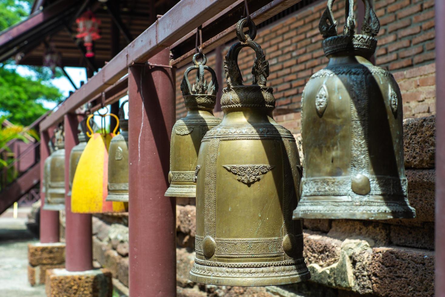 Selective focus on brass bells hanging on the steel bar at Buddhism temple photo