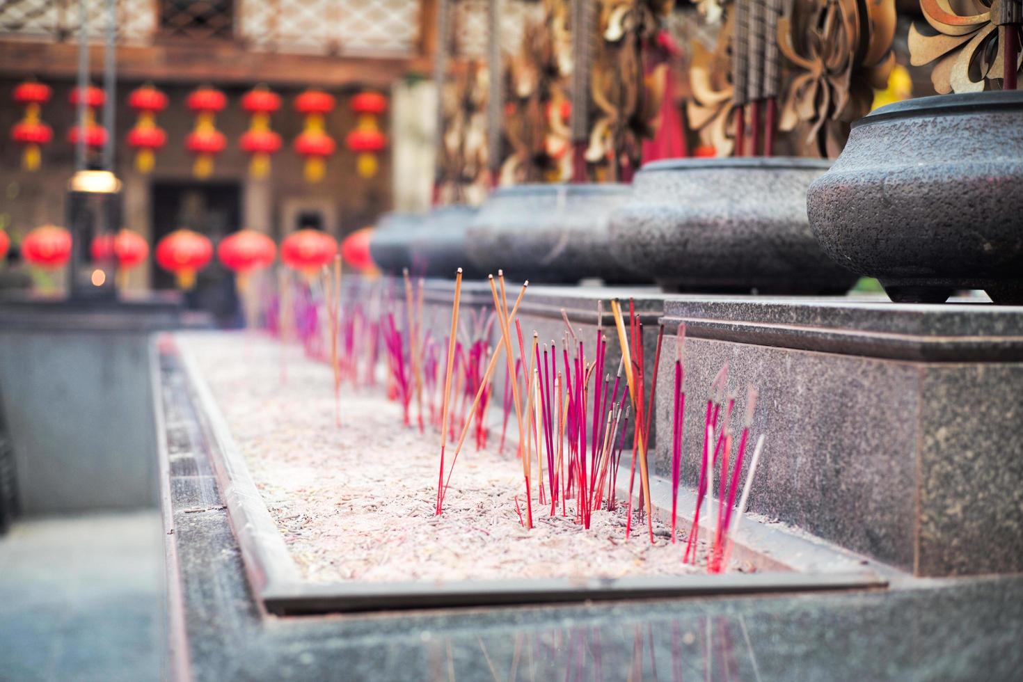 Selective focus on the bundle of fired incenses put in a sand tray with a blurred crowd of incense sticks in the background photo