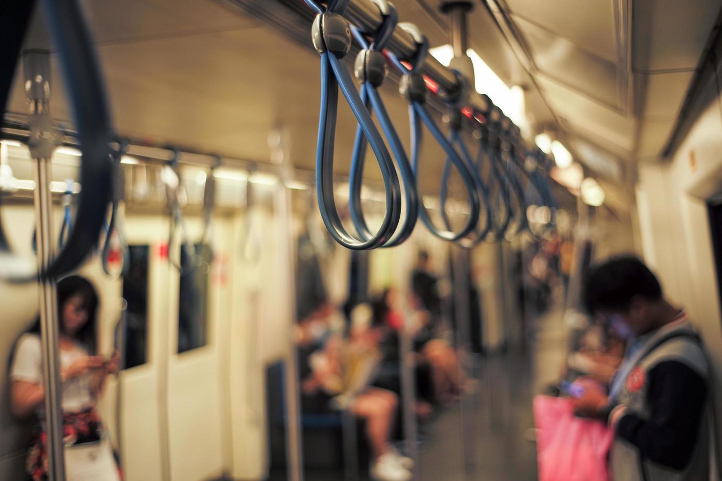 El enfoque selectivo en el grupo de pasamanos en el interior del tren con pasajeros borrosos y luces bokeh en segundo plano. foto