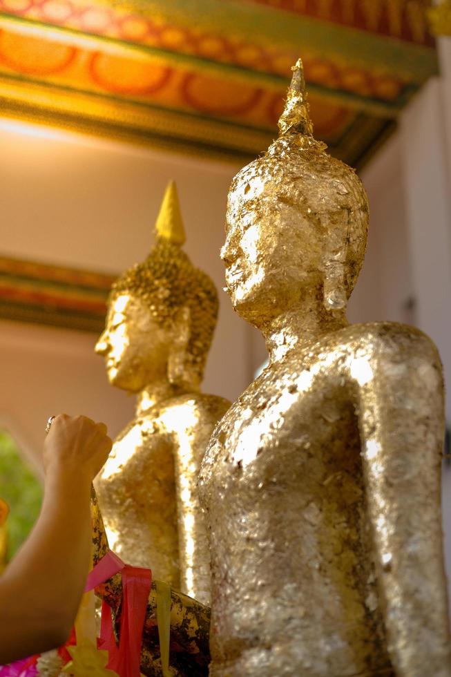 Hand of people hanging the flower garlands on the Buddhist statue's hand coated by golden leaf photo