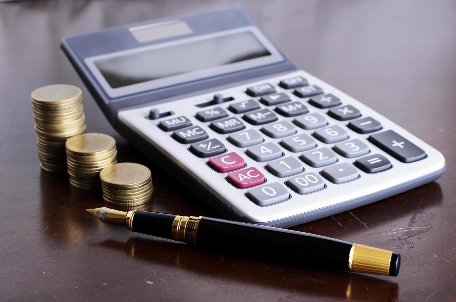 Pluma estilográfica y calculadora y pila de monedas en la mesa de madera para el concepto de dinero de préstamo foto