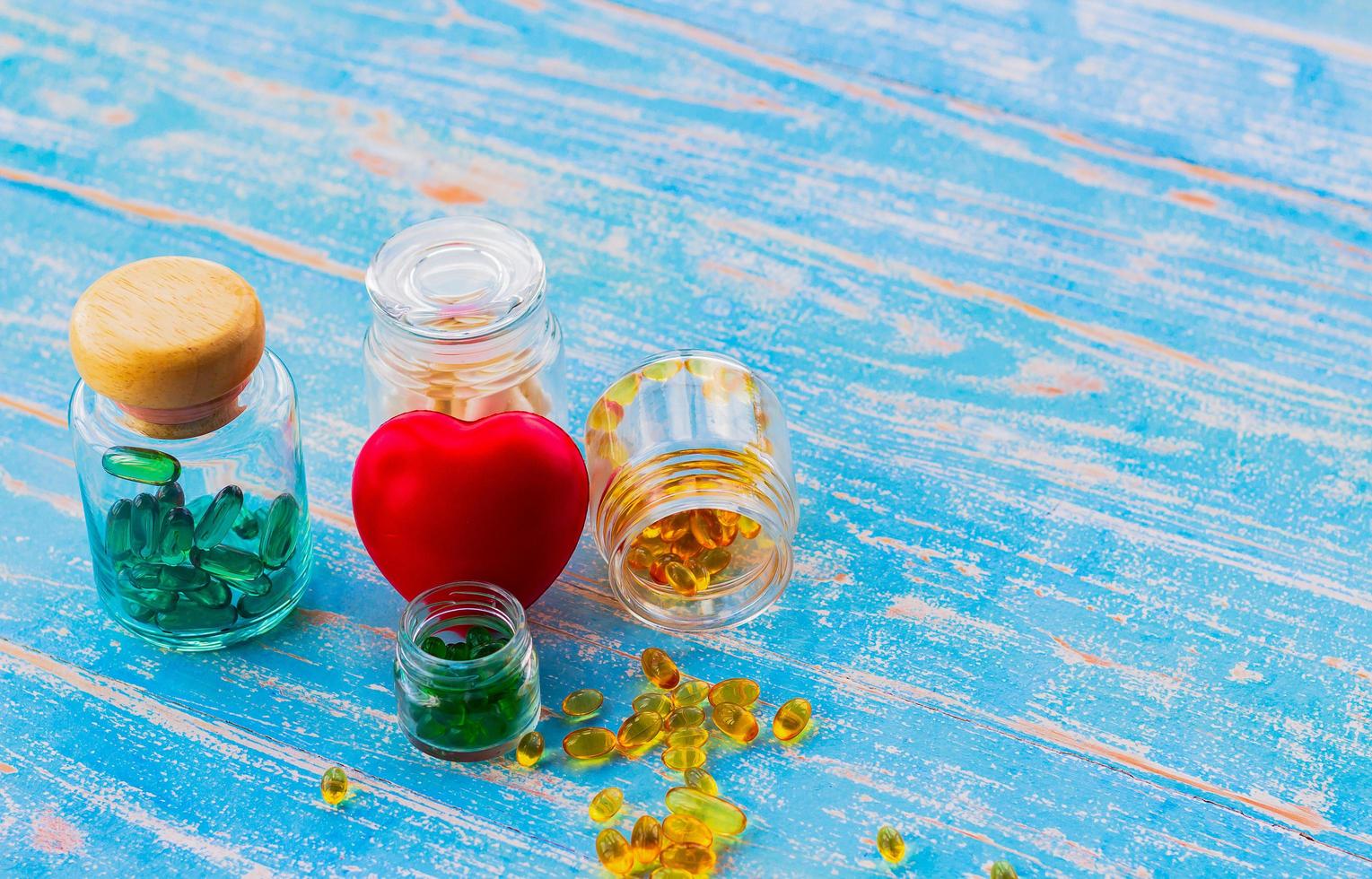 aceite de pescado en una botella de vidrio colocada sobre un piso de madera y un corazón rojo con espacio de copia. conceptos médicos y de atención de la salud foto