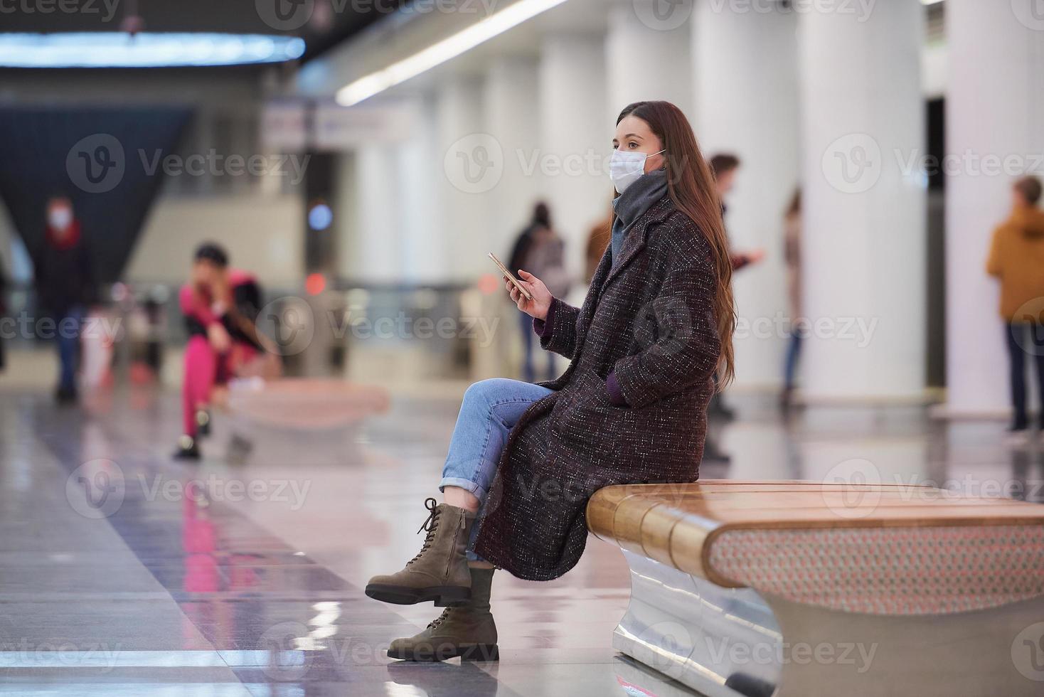 una mujer con una mascarilla médica está esperando un tren y sosteniendo un teléfono inteligente foto