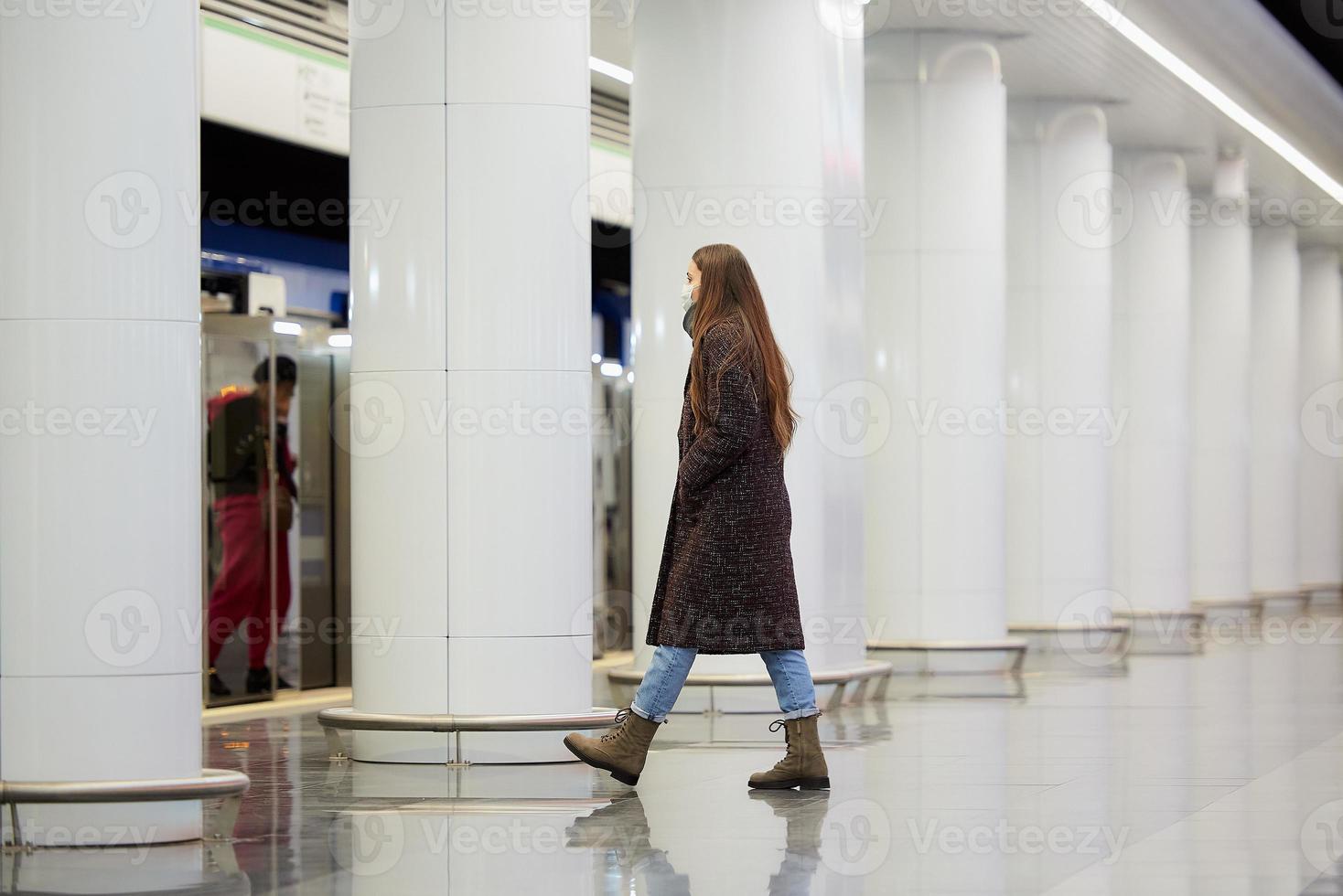 una niña con una mascarilla quirúrgica mantiene la distancia social en una estación de metro foto