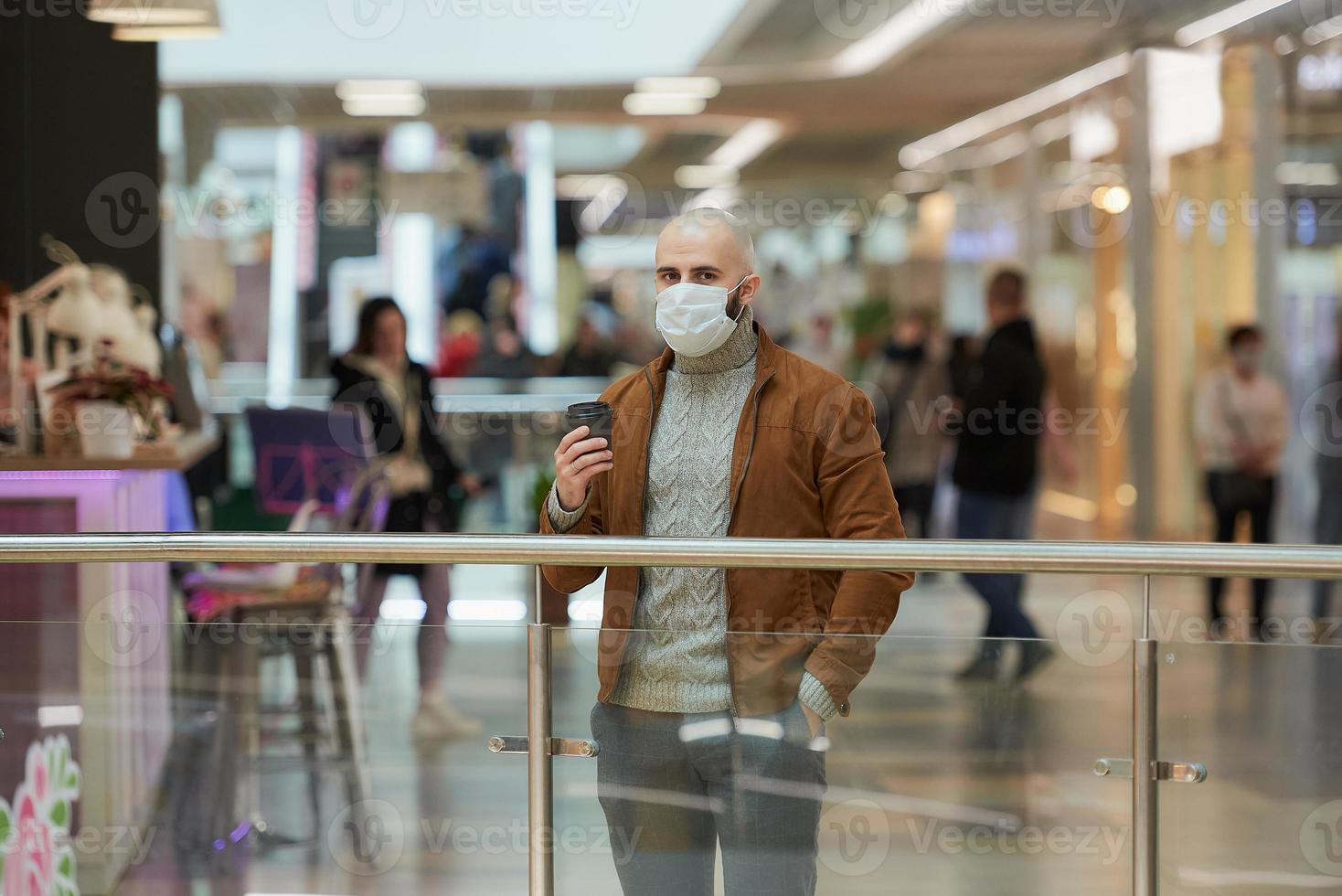 A man in a face mask is holding a cup of coffee in the shopping center photo