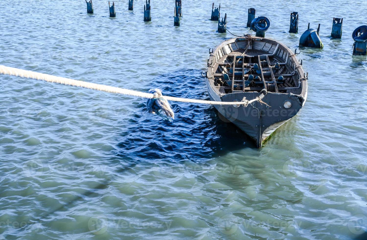 Gray fishing boat tied with a rope in blue-green water photo