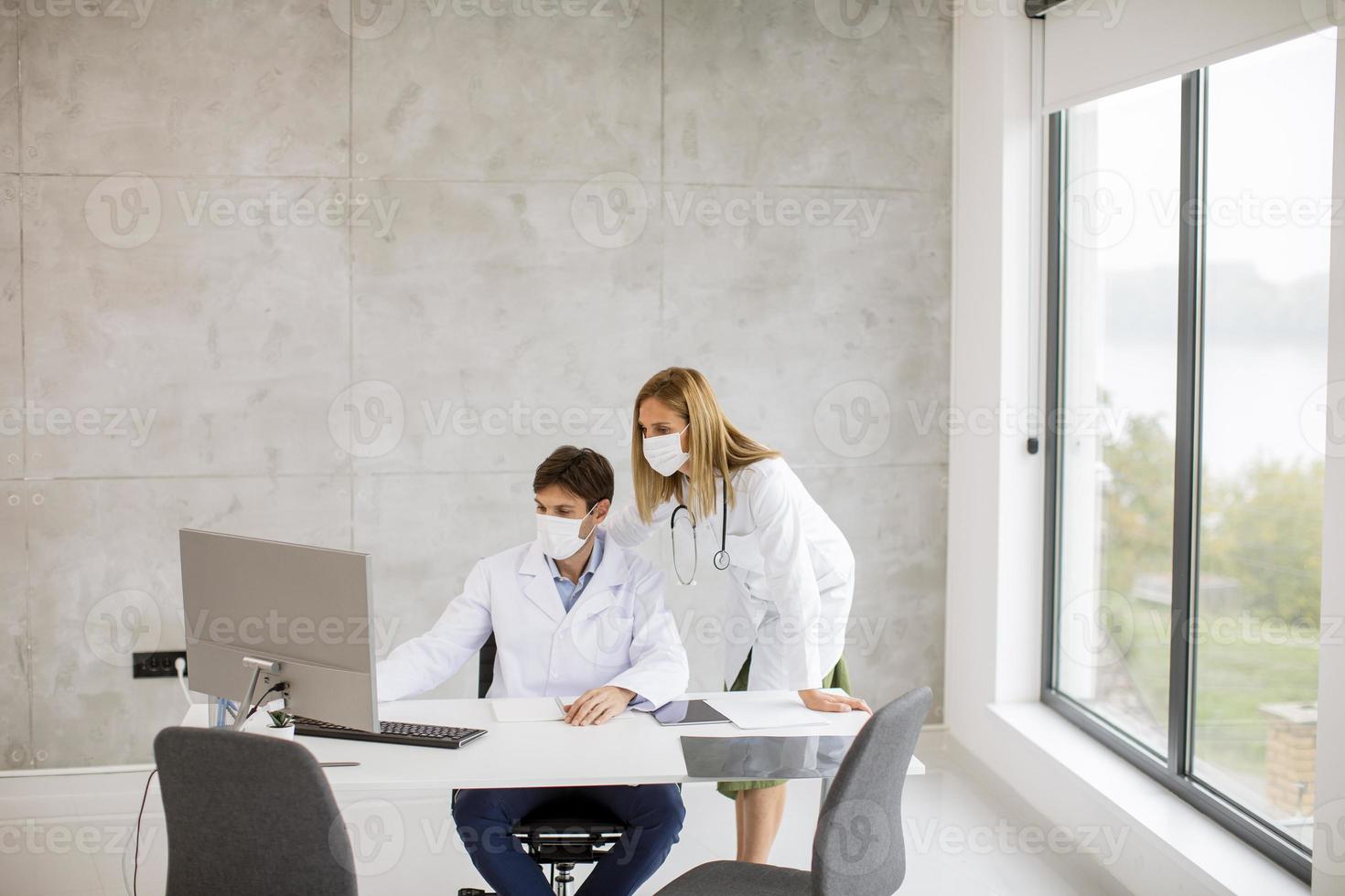 dos médicos que trabajan en una computadora mientras usan máscaras foto