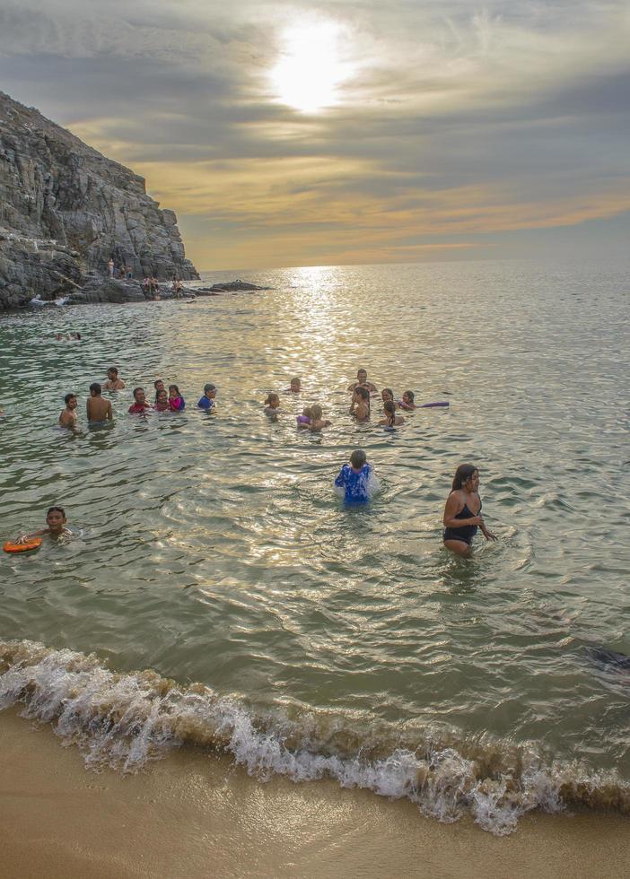 People enjoying the summer vacation in Punta Lobos beach in Todos Santos, Baja California Sur Mexico with the sunset on a cloudy sky and a mountain in the background photo