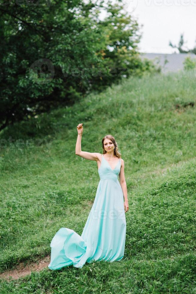 niña feliz en un vestido largo turquesa en un parque verde foto