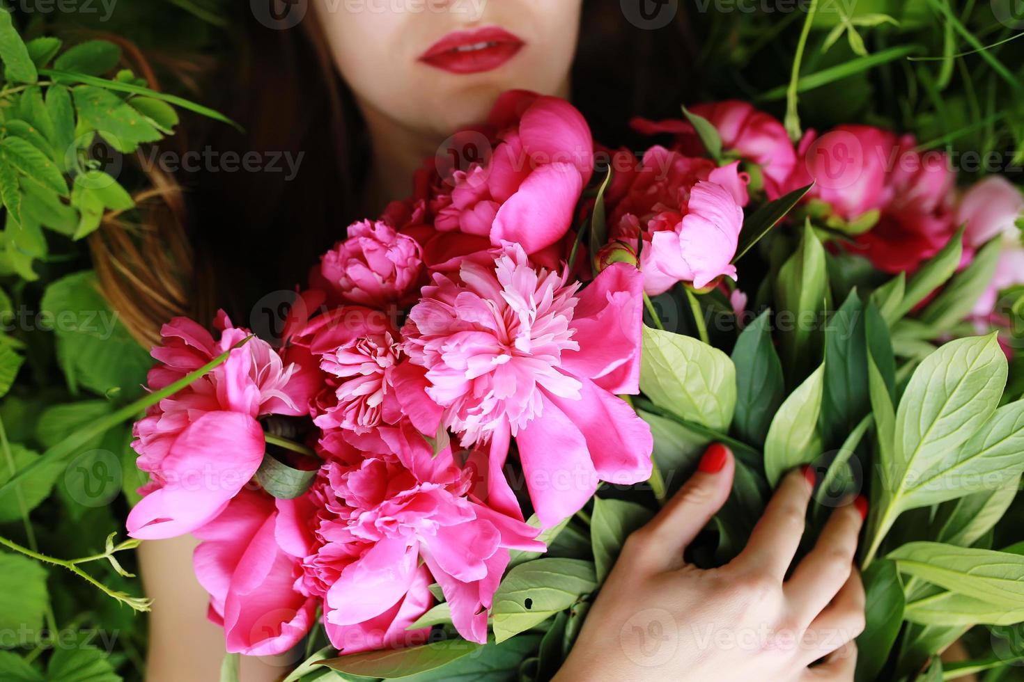 Beautiful young woman lies among peonies photo