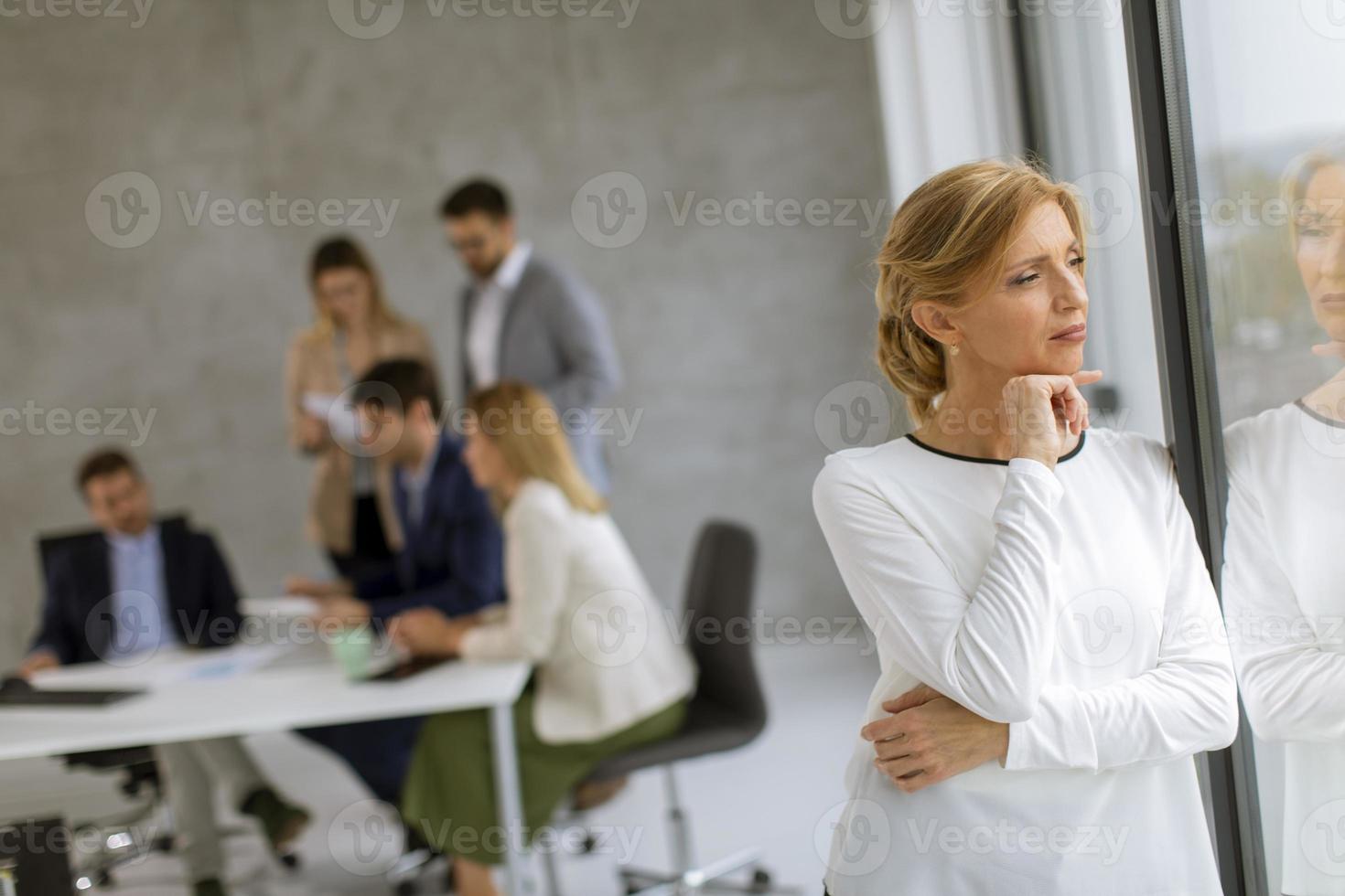 Woman looking out window with a business meeting behind her photo