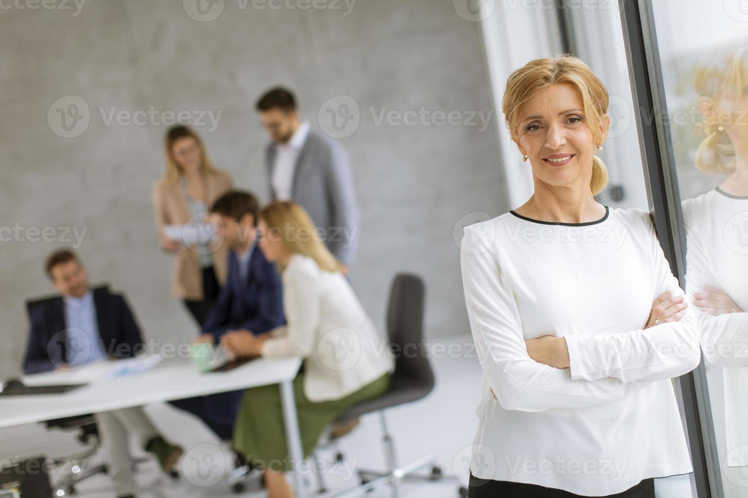 Woman leaning against a window with coworkers in the background photo