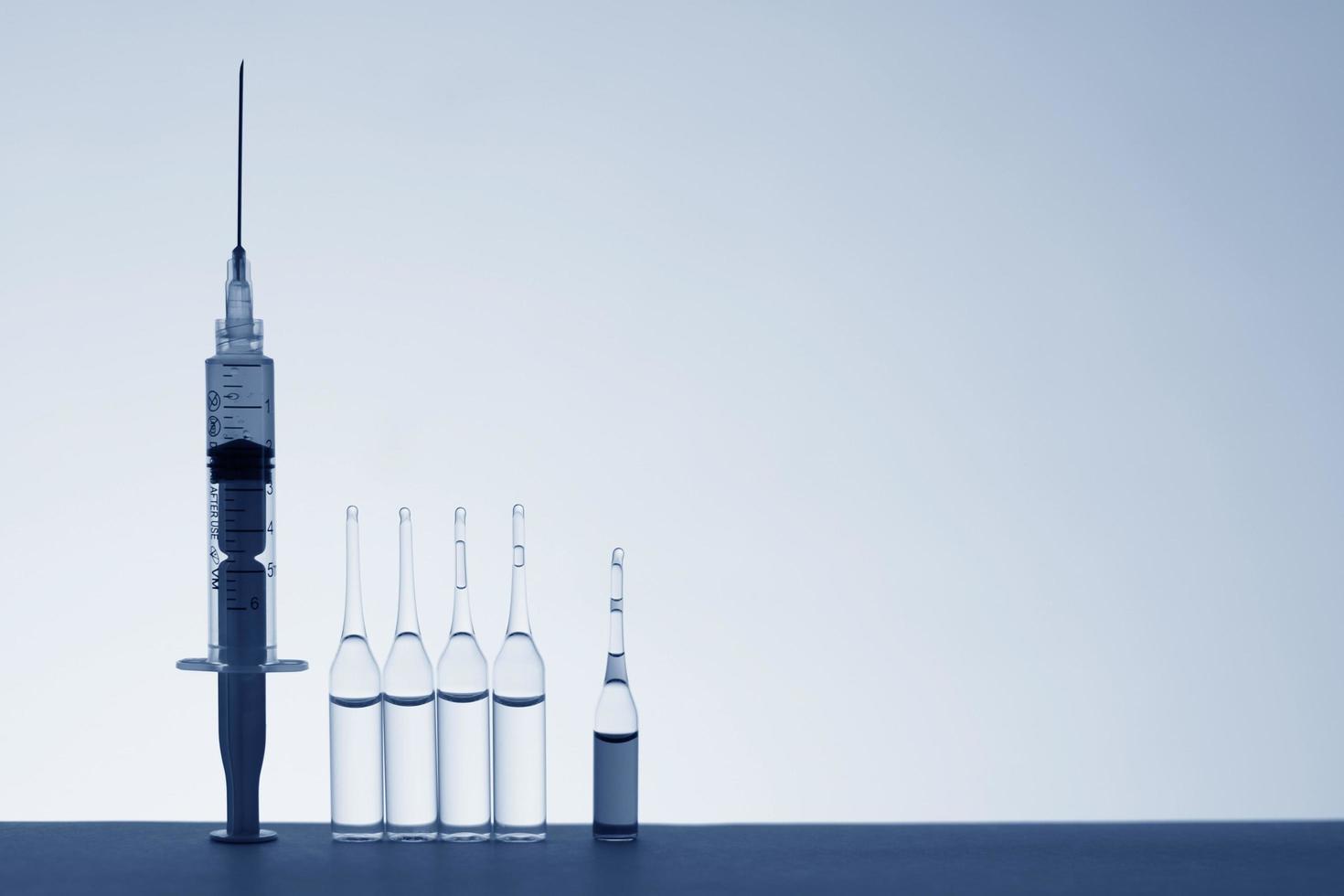 Backlit silhouettes of a syringe and vaccination tubes in blue monochrome photo