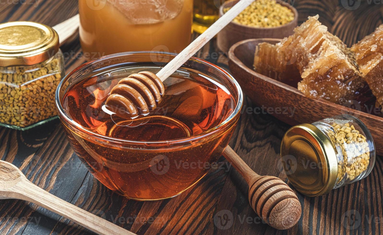 Honey in glass jar with honey dipper over wooden background photo