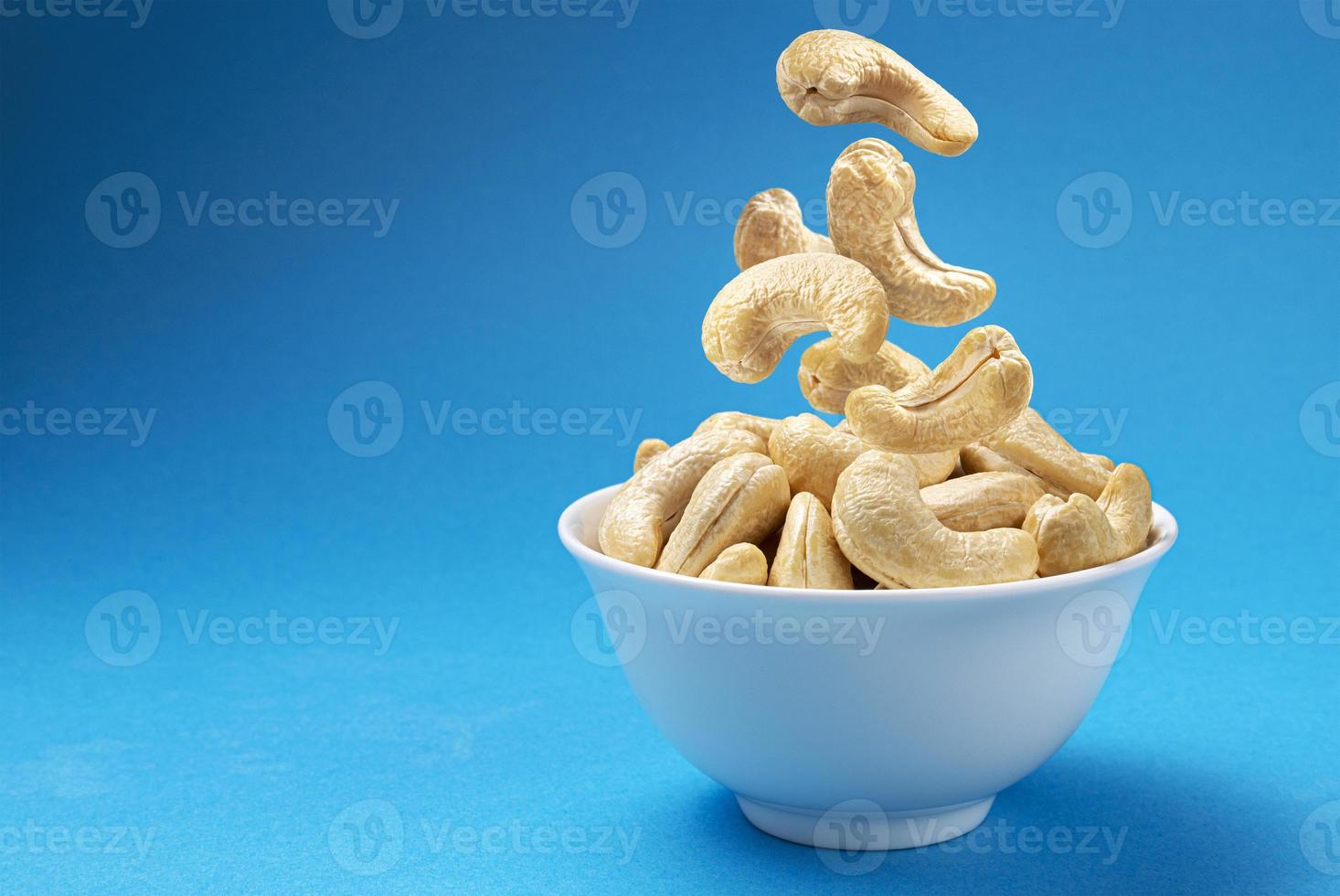 Falling cashew nuts into bowl on blue background photo