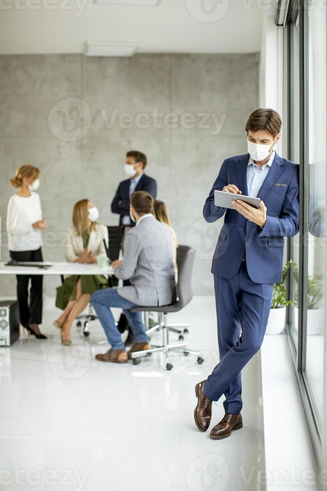 Man leaning against a window while using a tablet and wearing a mask photo