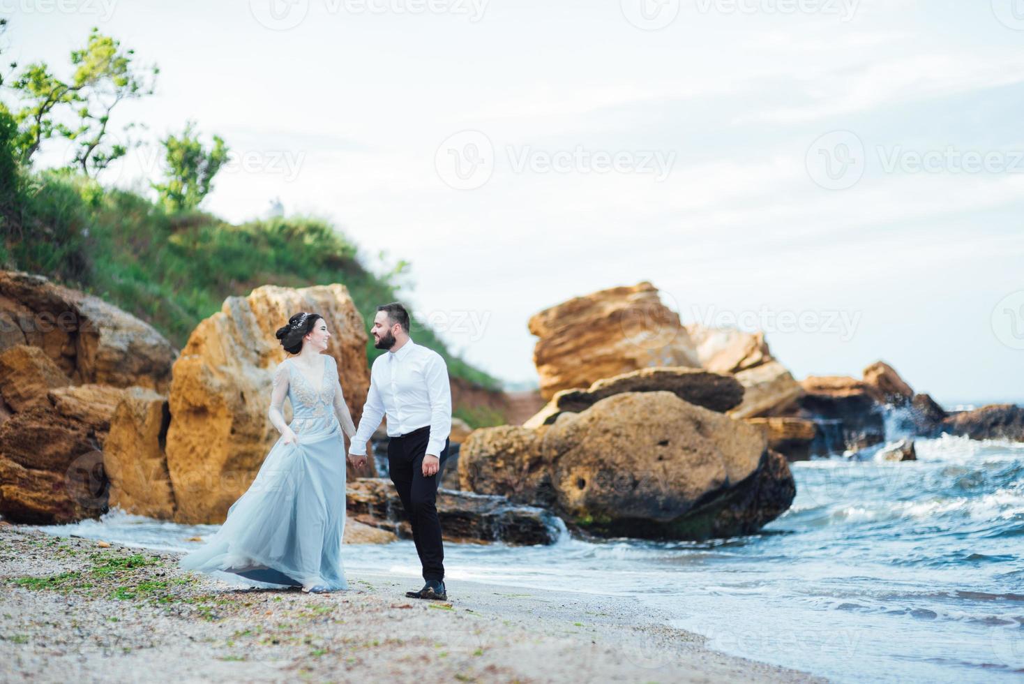 novia en un vestido azul con el novio caminando por la orilla del mar foto