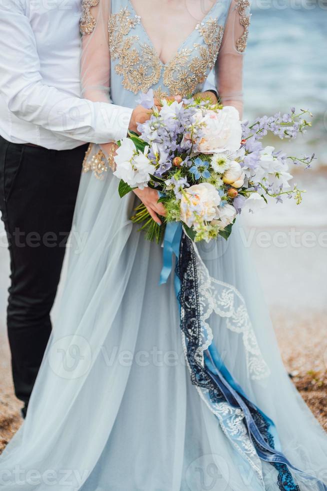 Bride in a blue dress with groom walking along the ocean shore photo