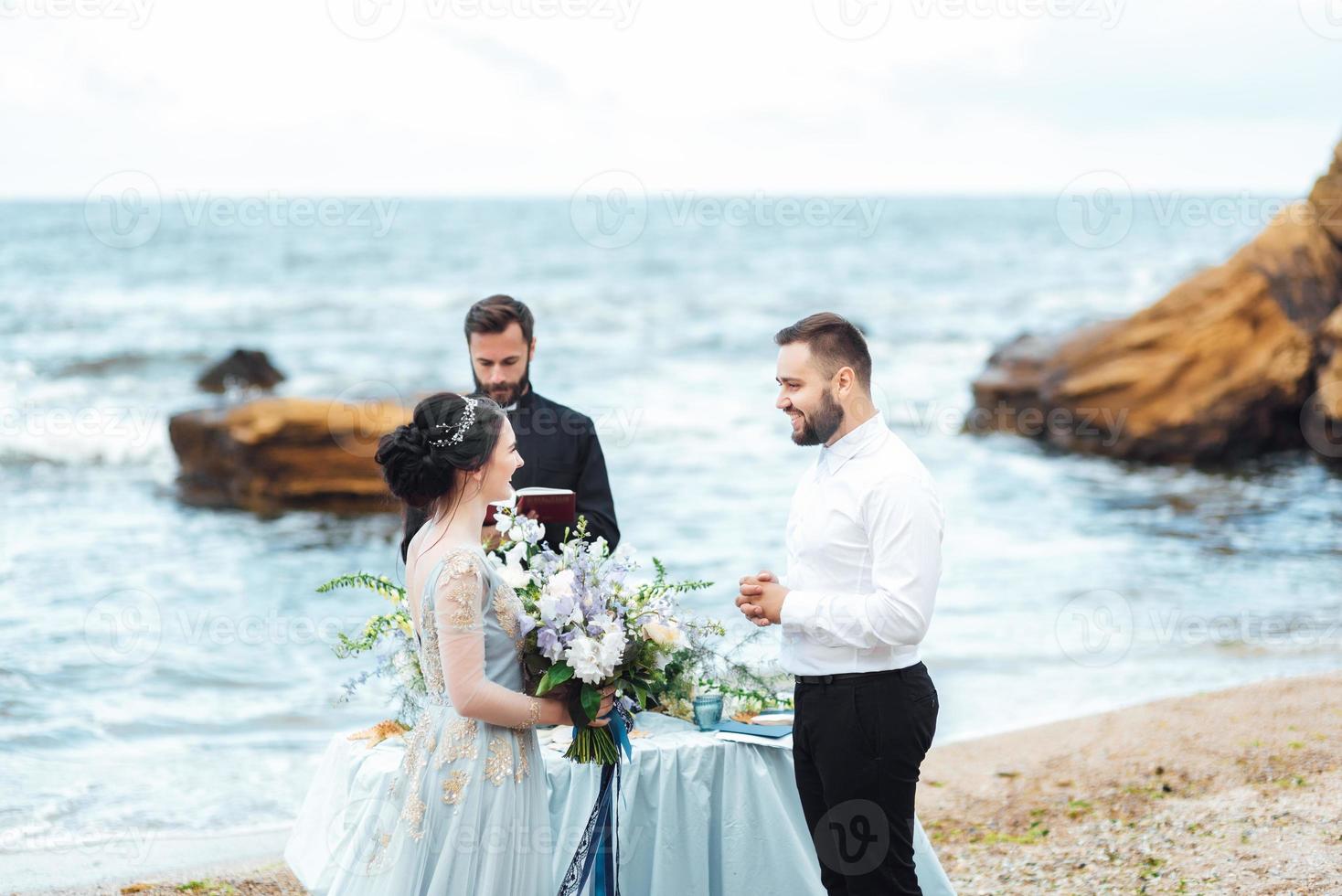 Wedding couple on the ocean with a priest photo