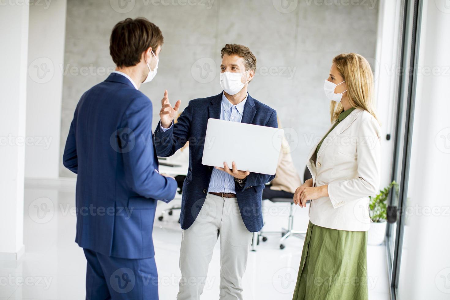 Tres profesionales enmascarados discutiendo con un portátil. foto