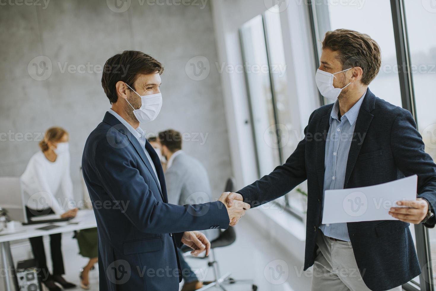 Two masked businessmen shaking hands in agreement photo