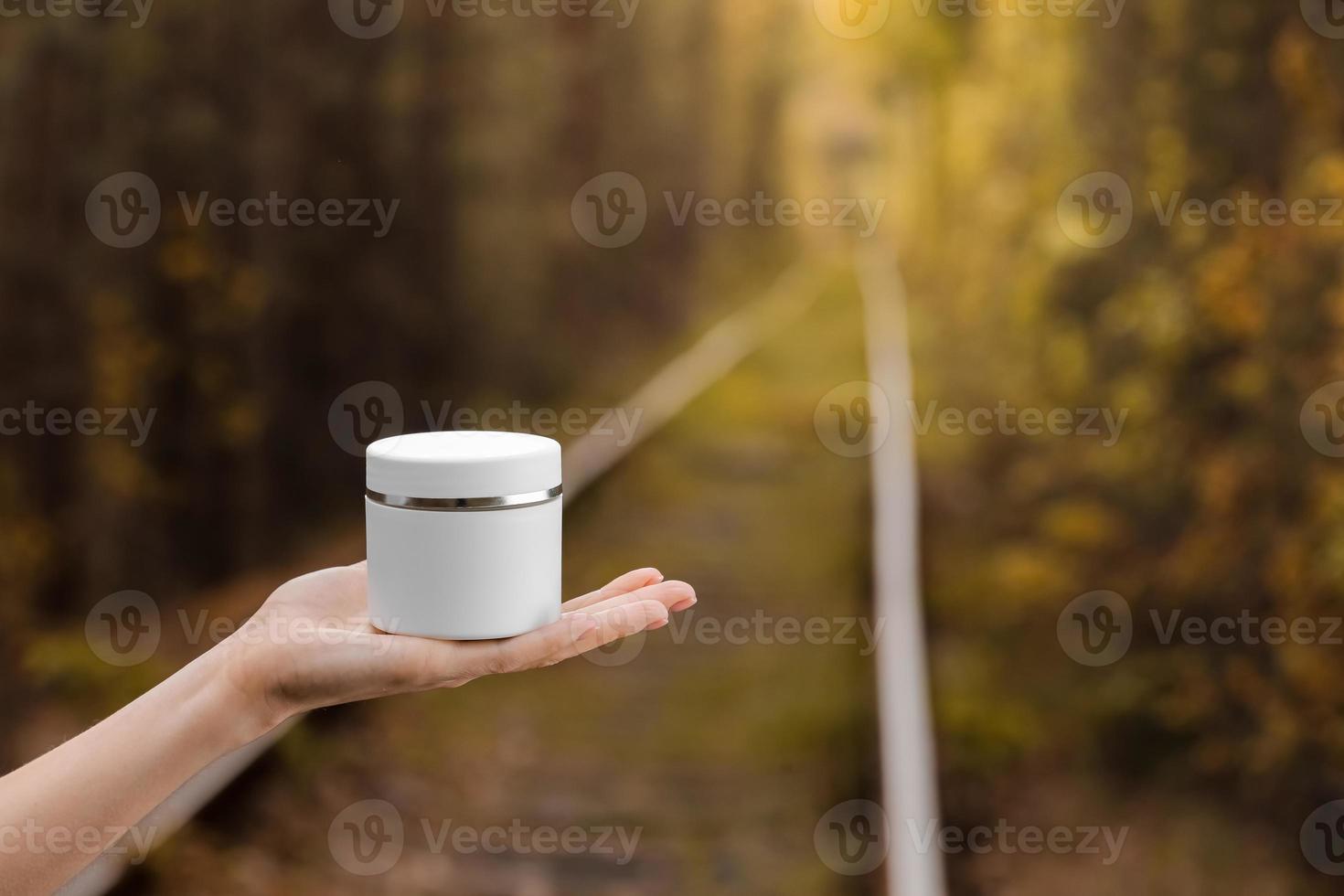 Mano femenina joven sostiene un tarro de crema en otoño de fondo natural foto