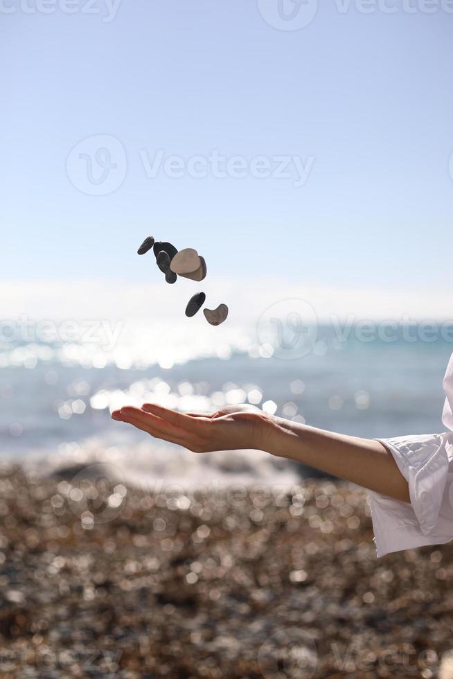 Mano femenina lanza un guijarro en su mano contra el cielo azul y la playa foto