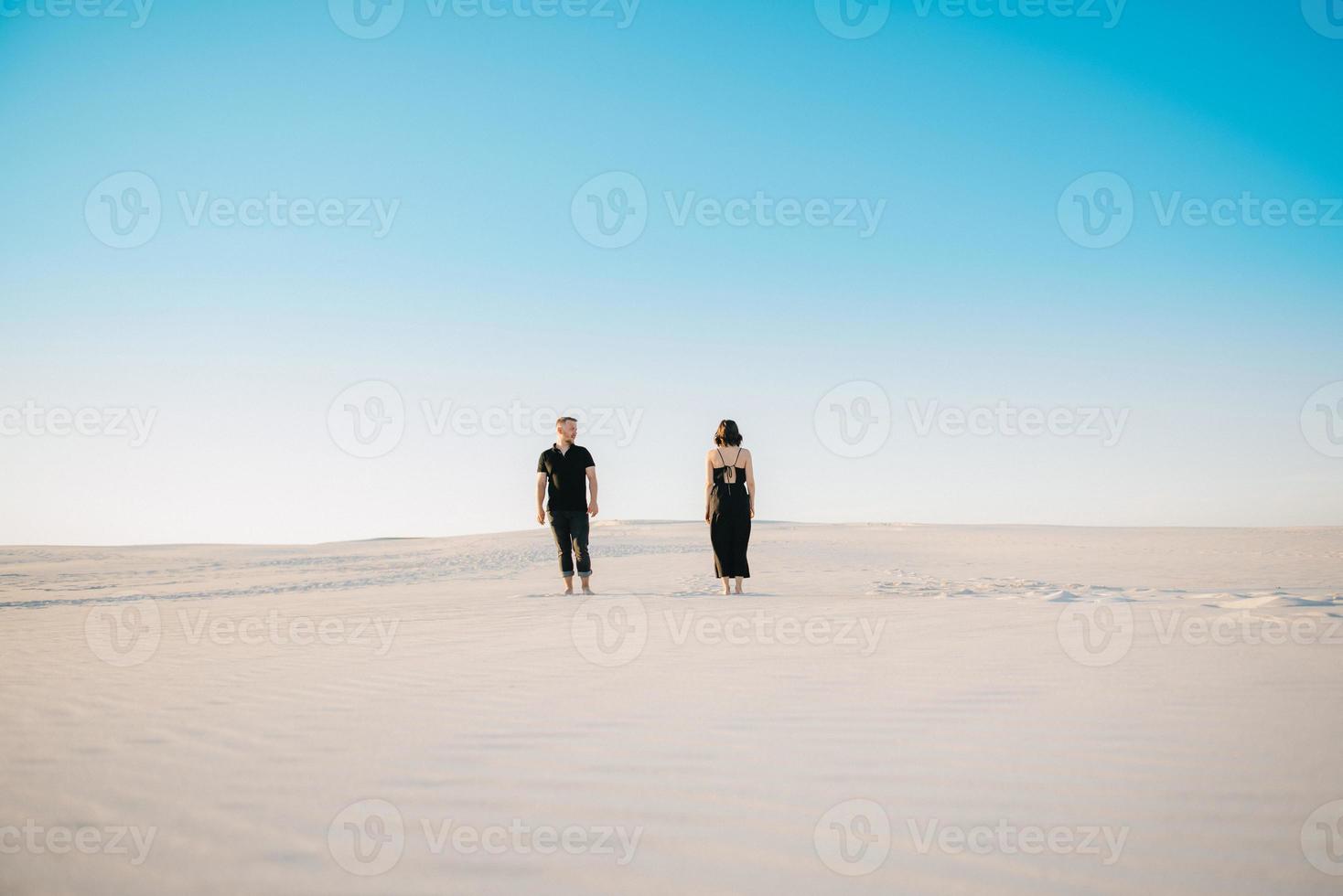 Pareja joven un chico y una chica con emociones alegres en ropa negra caminan por el desierto blanco foto