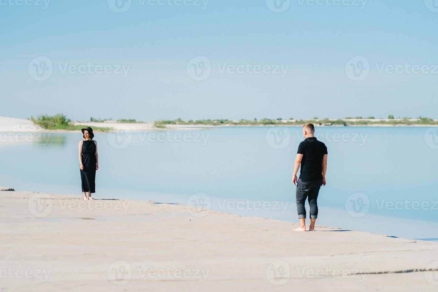 Pareja joven un chico con una chica vestida de negro están caminando sobre la arena blanca foto