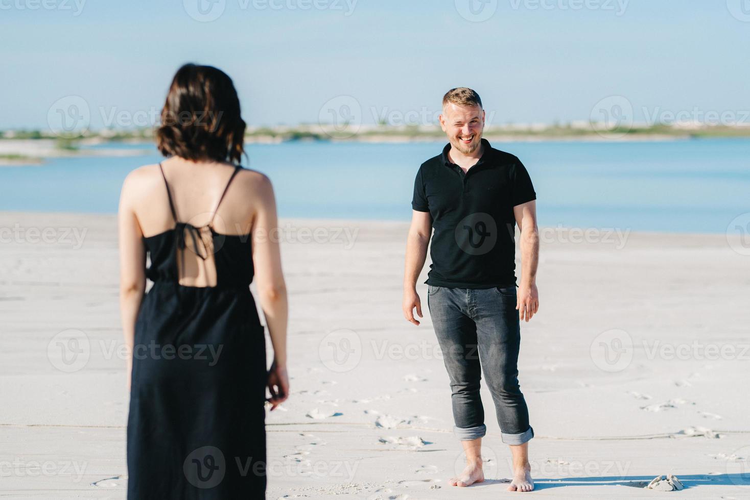 Young couple a guy with a girl in black clothes are walking on the white sand photo