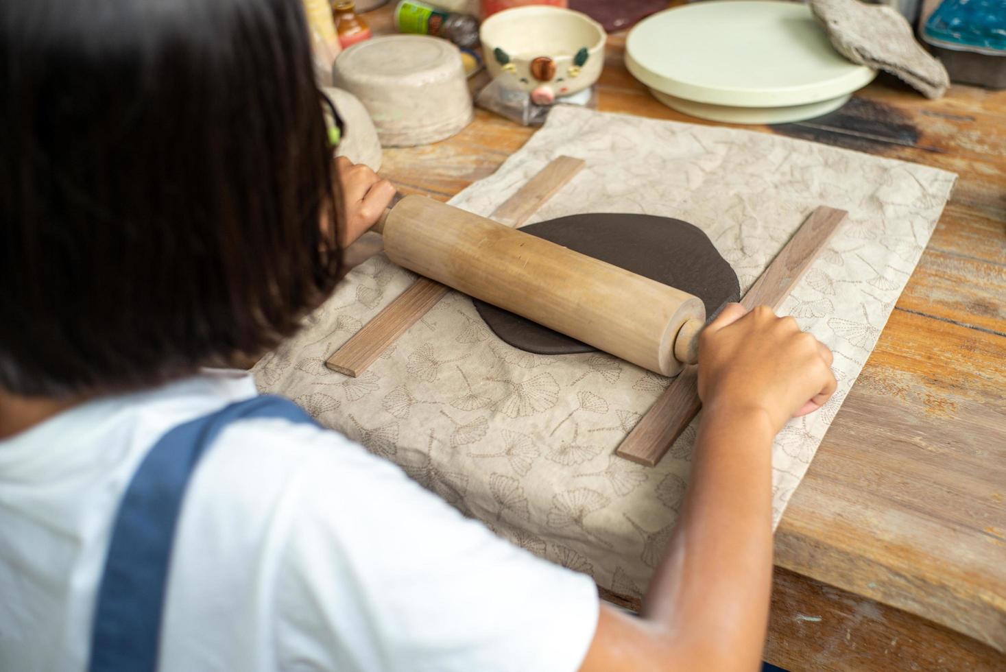 Closeup hands of girl using the rolling pin on the clay during molding workshop class photo